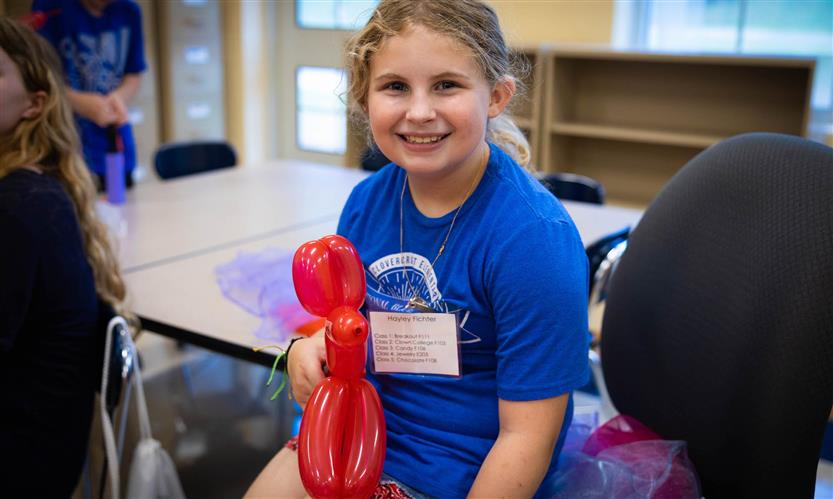 A girl wearing a blue shirt holds a red balloon animal